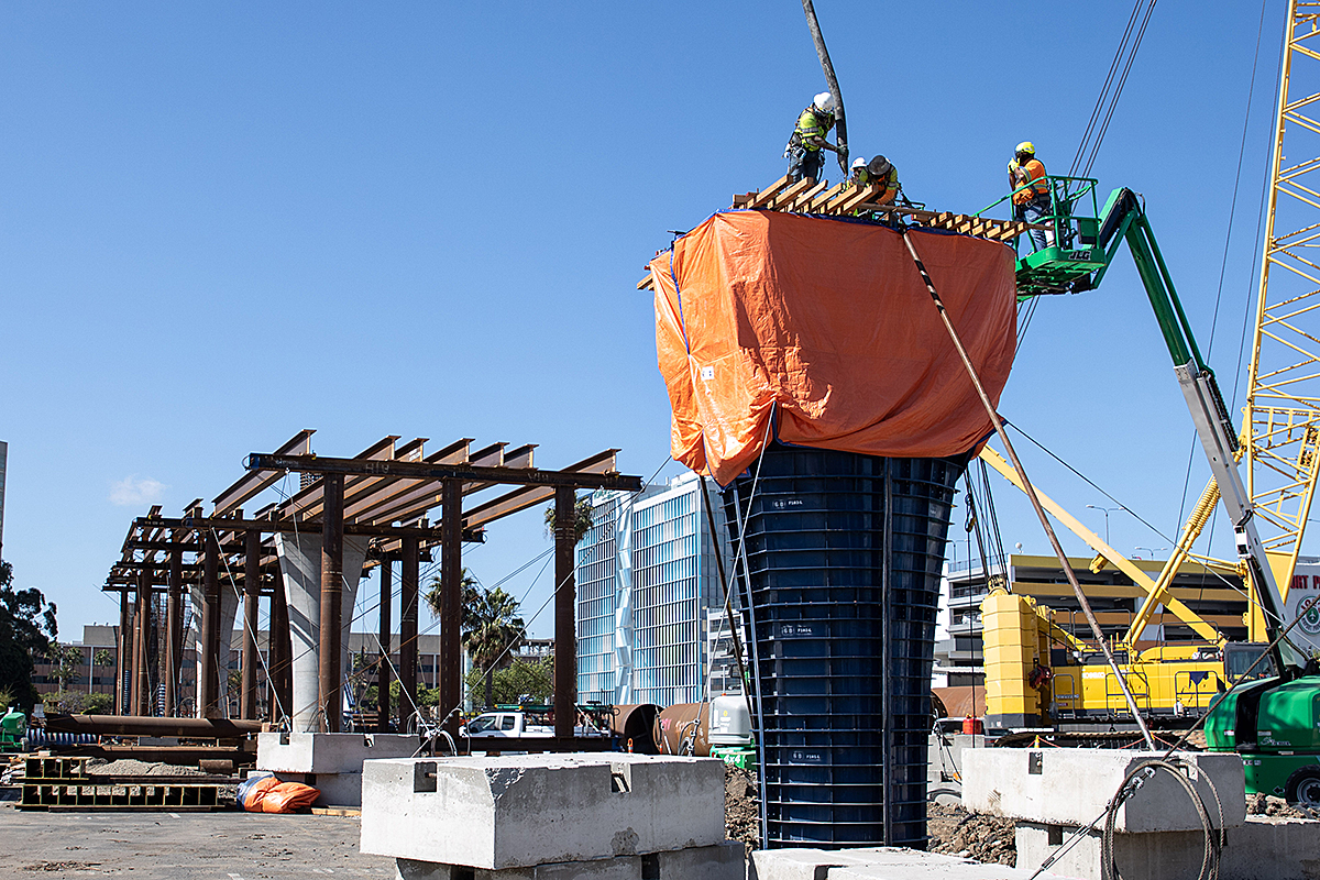 A crew places concrete into column formwork where the guideway approaches Century Boulevard.