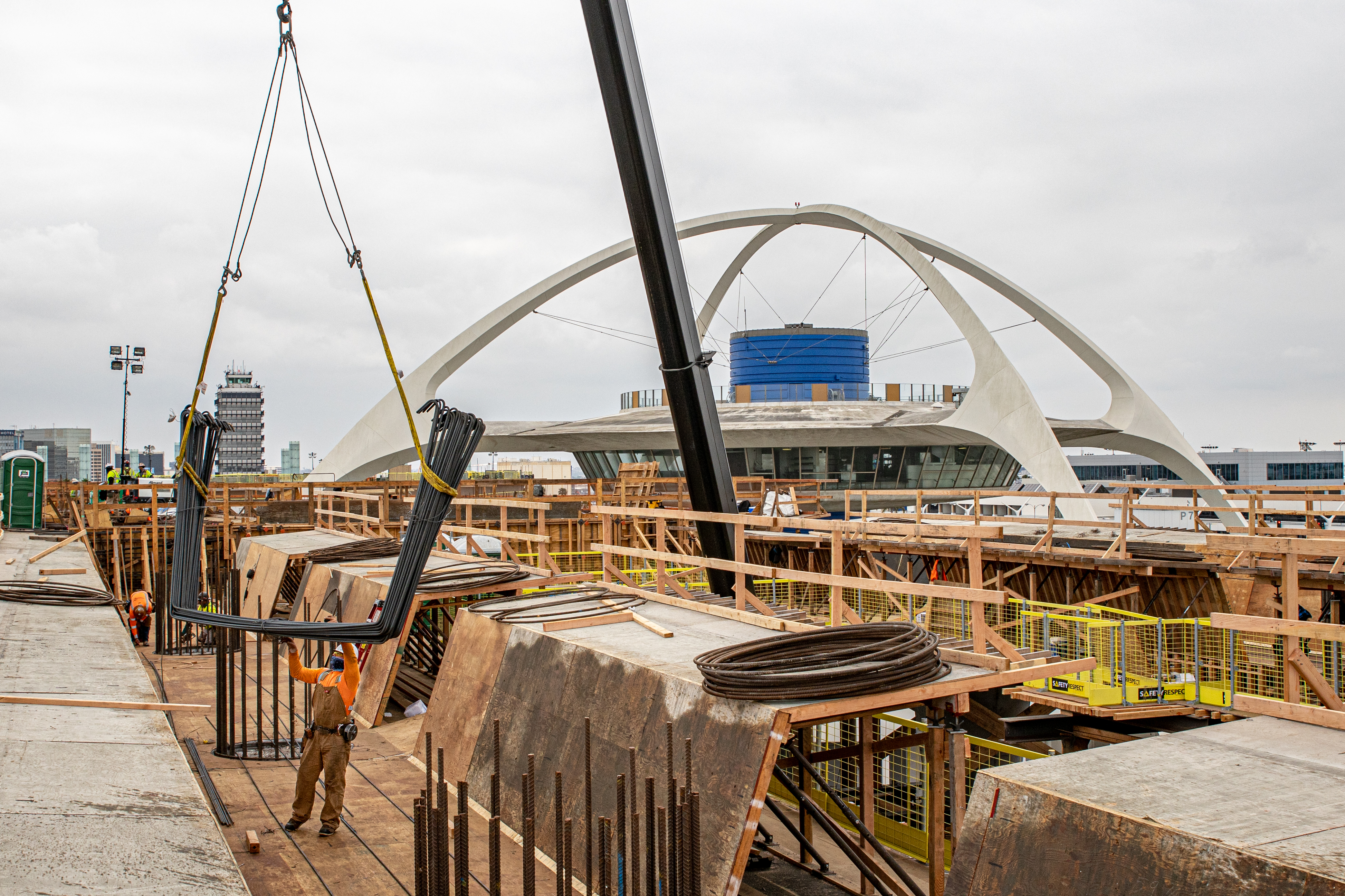 A crane is used to lift materials to the top of the falsework as an ironworker prepares to reinforce the guideway deck prior to concrete placement.