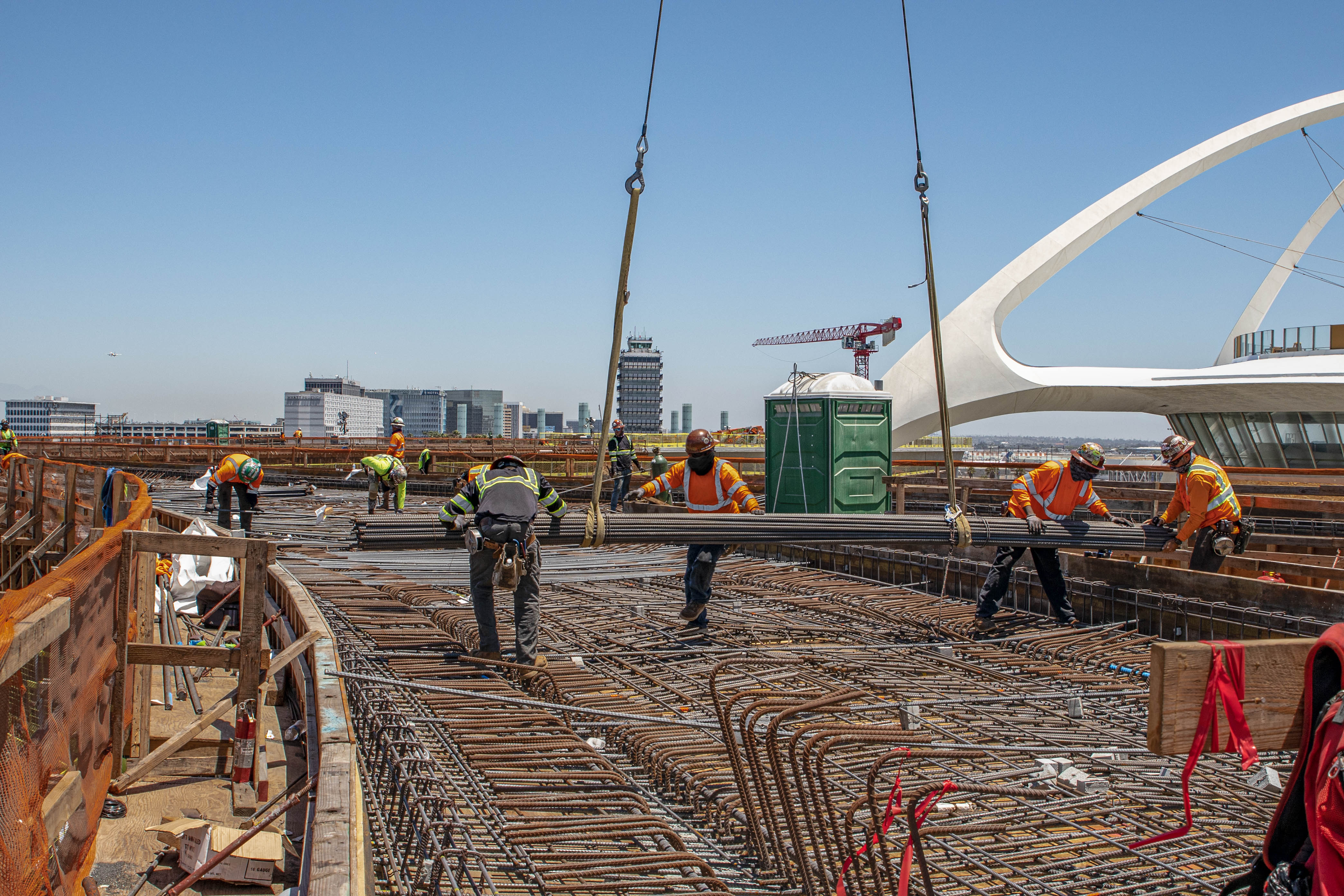 Crews guide a steel reinforcement bar bundle delivered to the guideway deck by crane. 